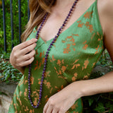 woman wearing a strappy green dress and a long beaded purple necklace 