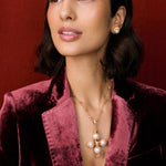 Model shot of lady wearing a gold cross pendant necklace and velvet blazer and gold ring. The necklace features pastel coloured agate gemstones, pearls and intricate filigree hung from a textured beaded chain.