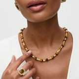 Close-up of a woman wearing a gold necklace and ring on a white background