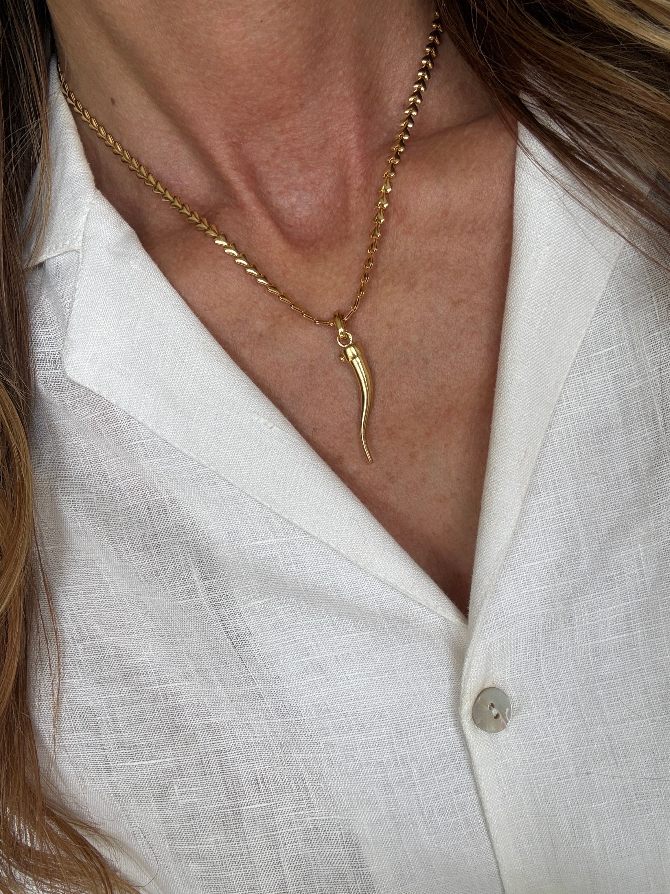 Close-up of a gold cornicello charm necklace worn by a person against a white shirt background