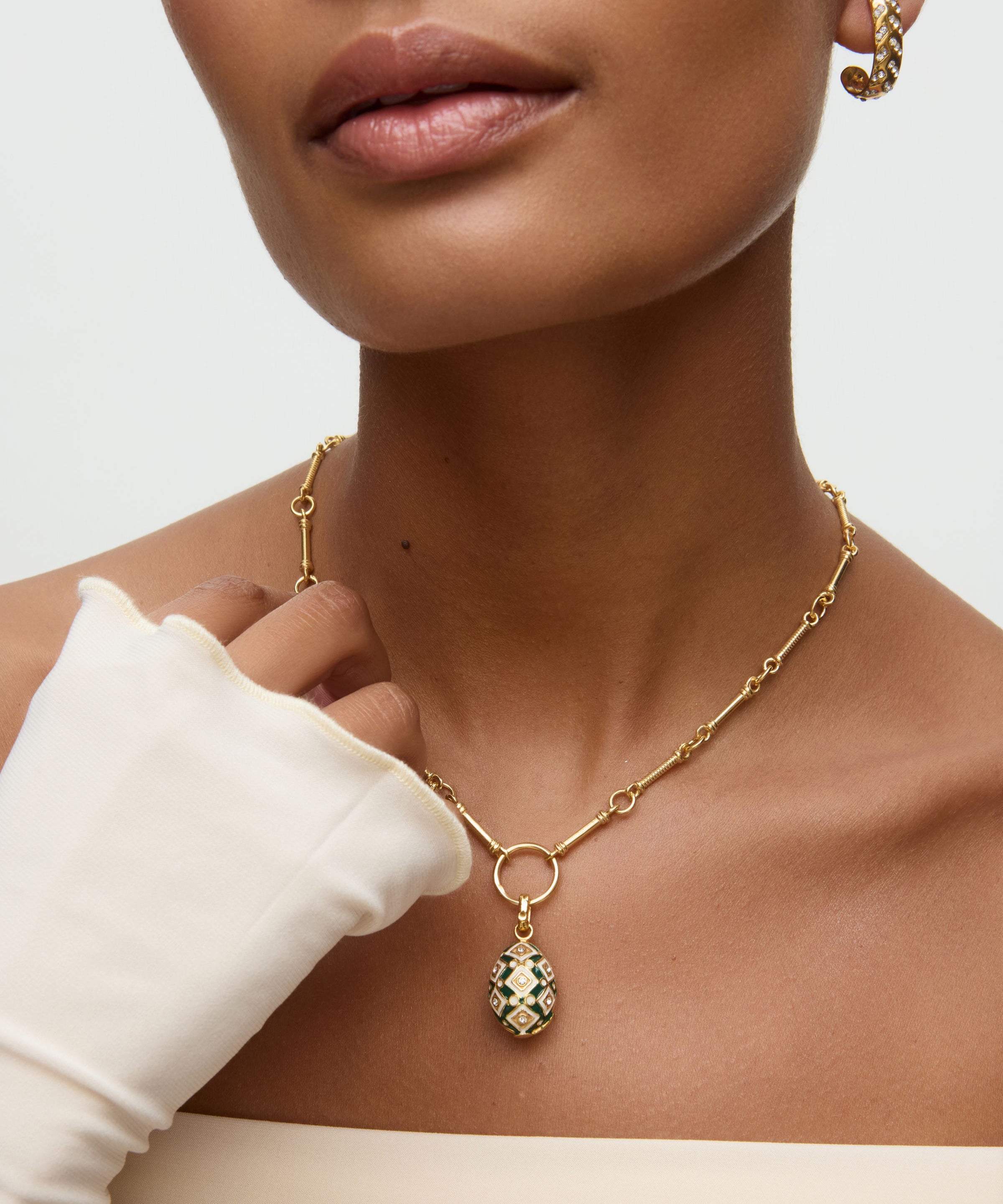 Gold necklace with a green and gold egg shaped pendant worn by a person against a neutral background