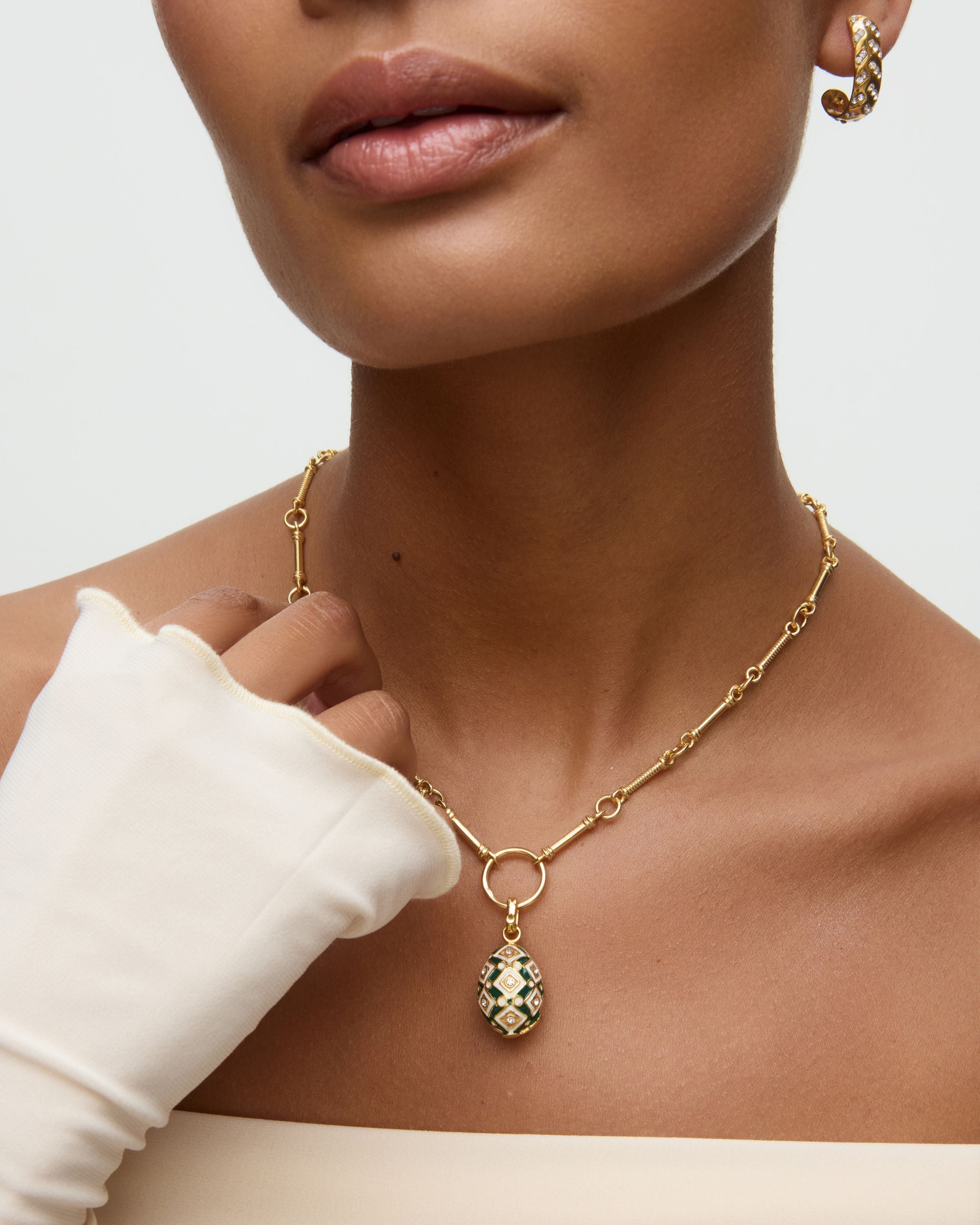 Gold necklace with a green and gold egg shaped pendant worn by a person against a neutral background