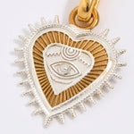 Heart-shaped pendant with eye design in gold and silver on a white background