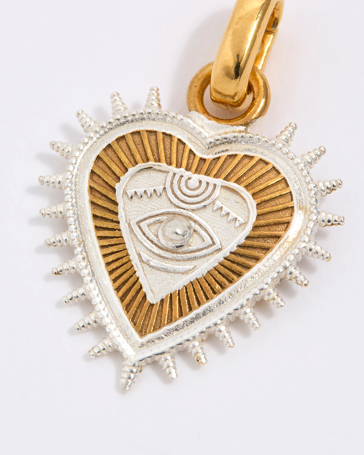 Heart-shaped pendant with eye design in gold and silver on a white background