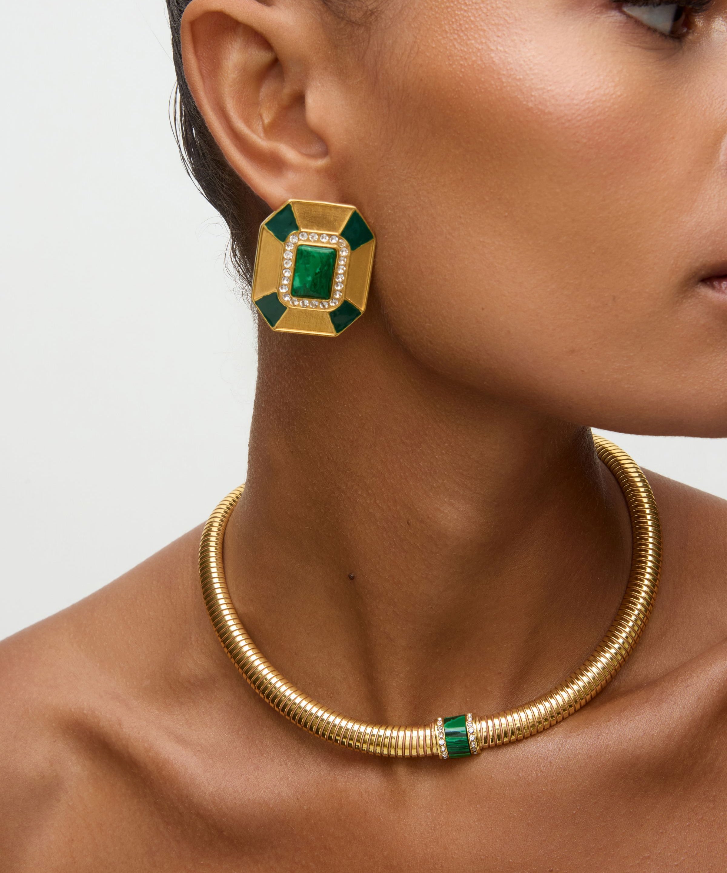 Close up side view of model shot wearing  statement gold and green malachite earrings with clear crystal embellished and matching necklace on a white background