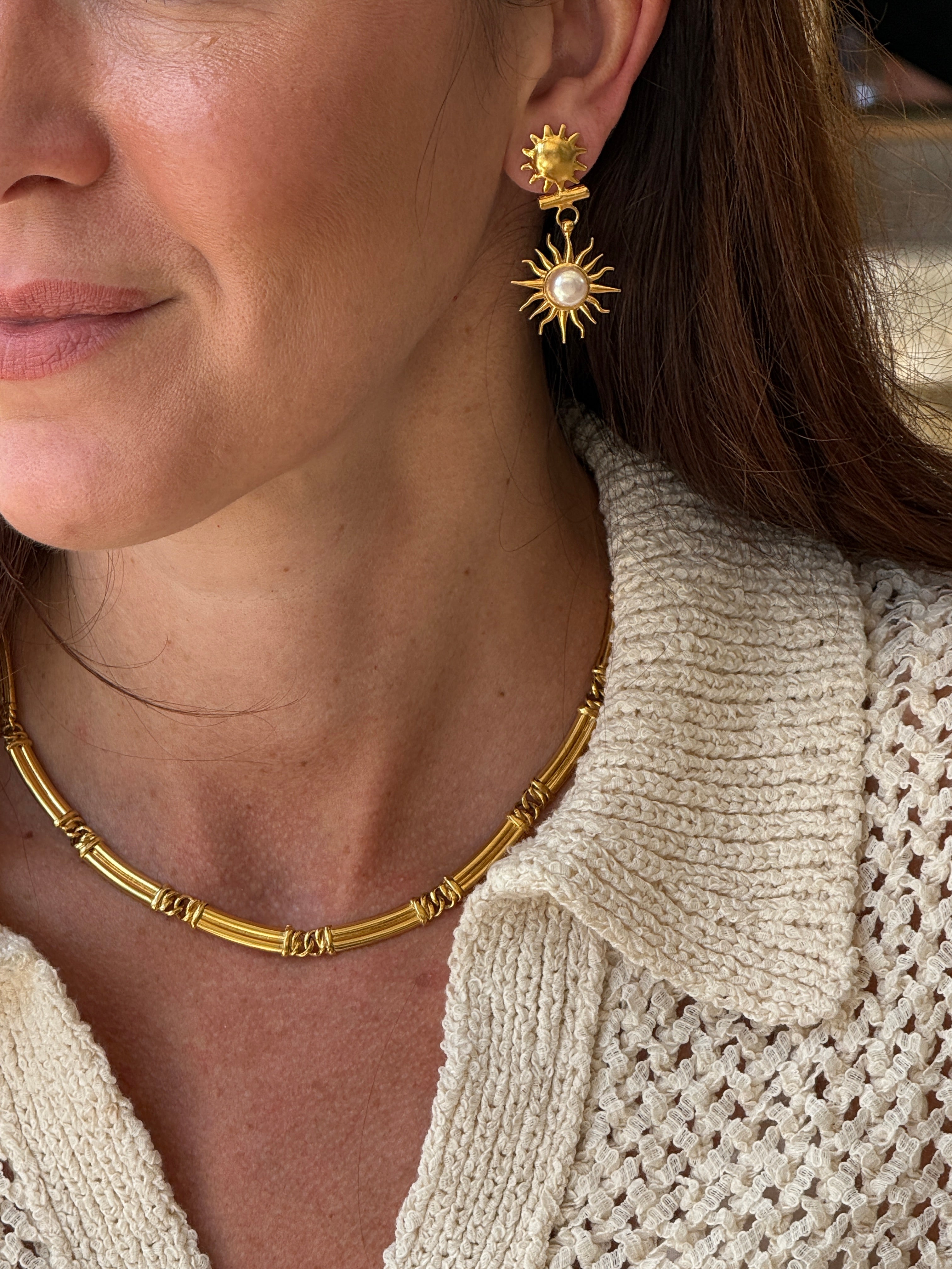 Close-up of a person wearing gold coloured necklace and earrings 