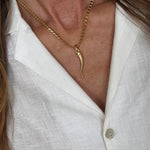Close-up of a gold cornicello charm necklace worn by a person against a white shirt background