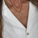 Close-up of a gold cornicello charm necklace worn by a person against a white shirt background