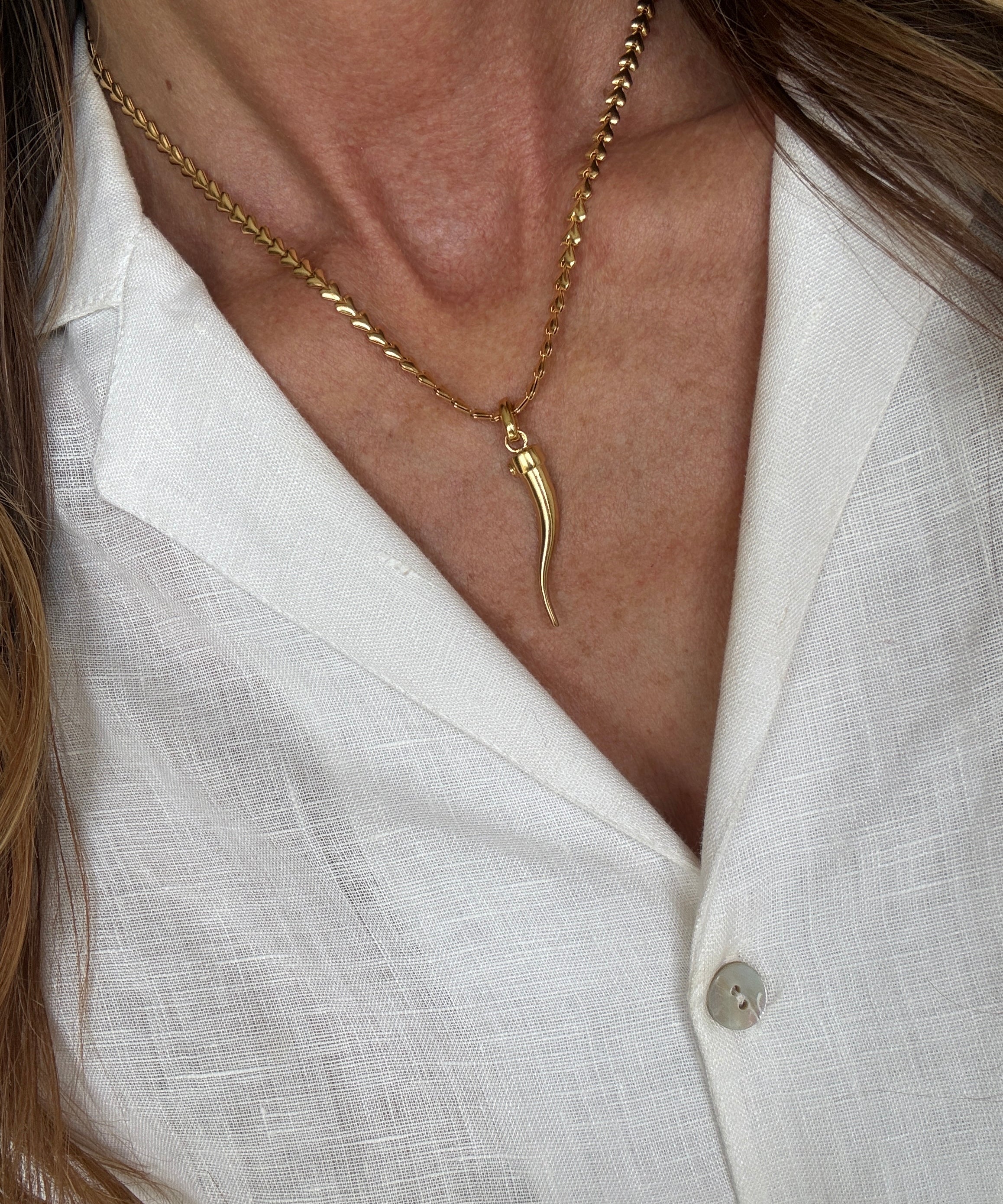 Close-up of a gold cornicello charm necklace worn by a person against a white shirt background