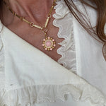 Close-up of a gold anklet with a pink bead on a white fabric background