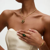 Woman wearing gold necklace with circular gold and onyx charm, green and onyx ring, and bracelet   on a neutral background