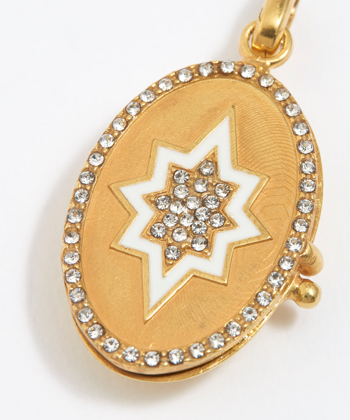 Oval Gold pendant with white start and crystals to centre of star and around the edge, on a white background