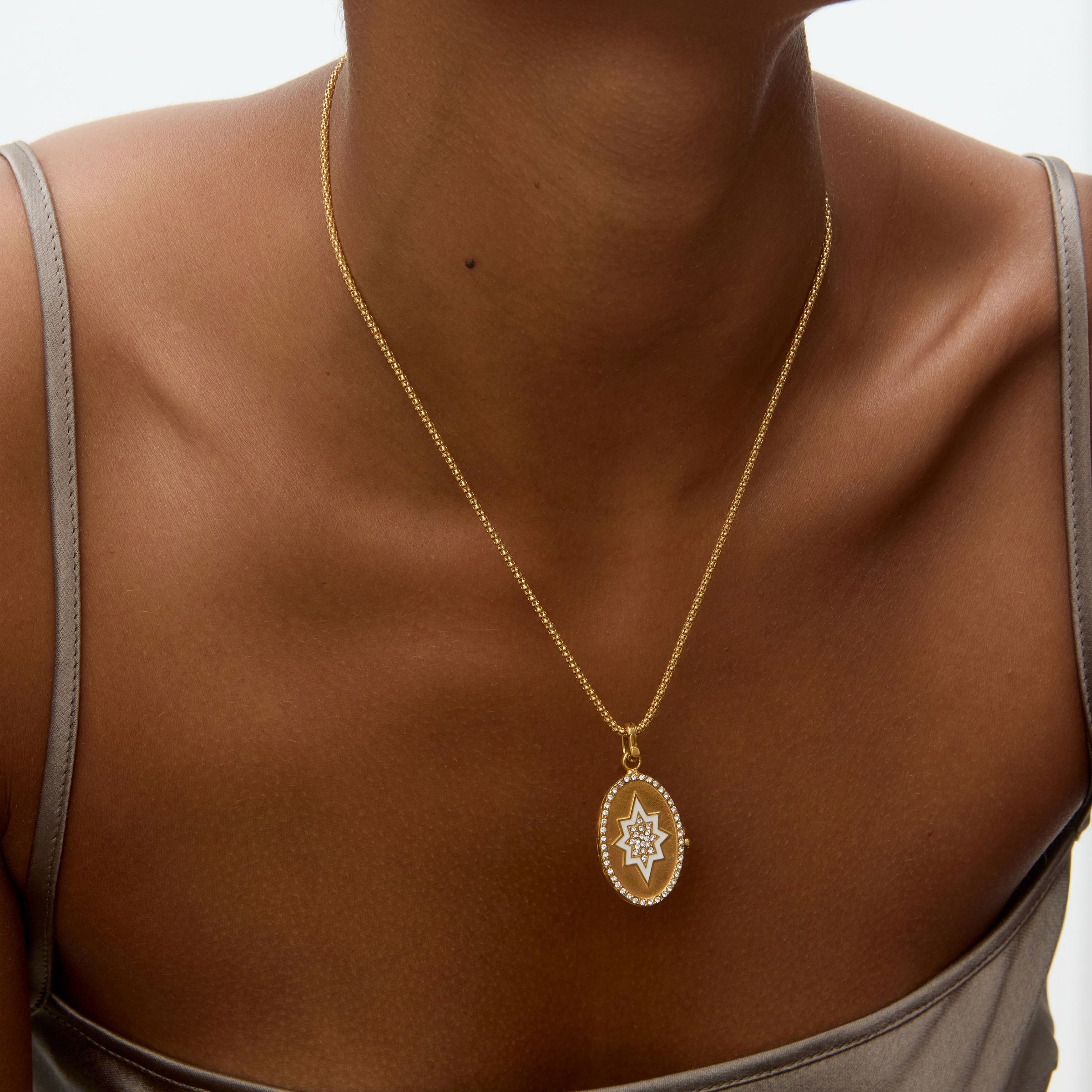 Gold necklace with a oval shaped locket pendant on a person wearing a gray top against a neutral background