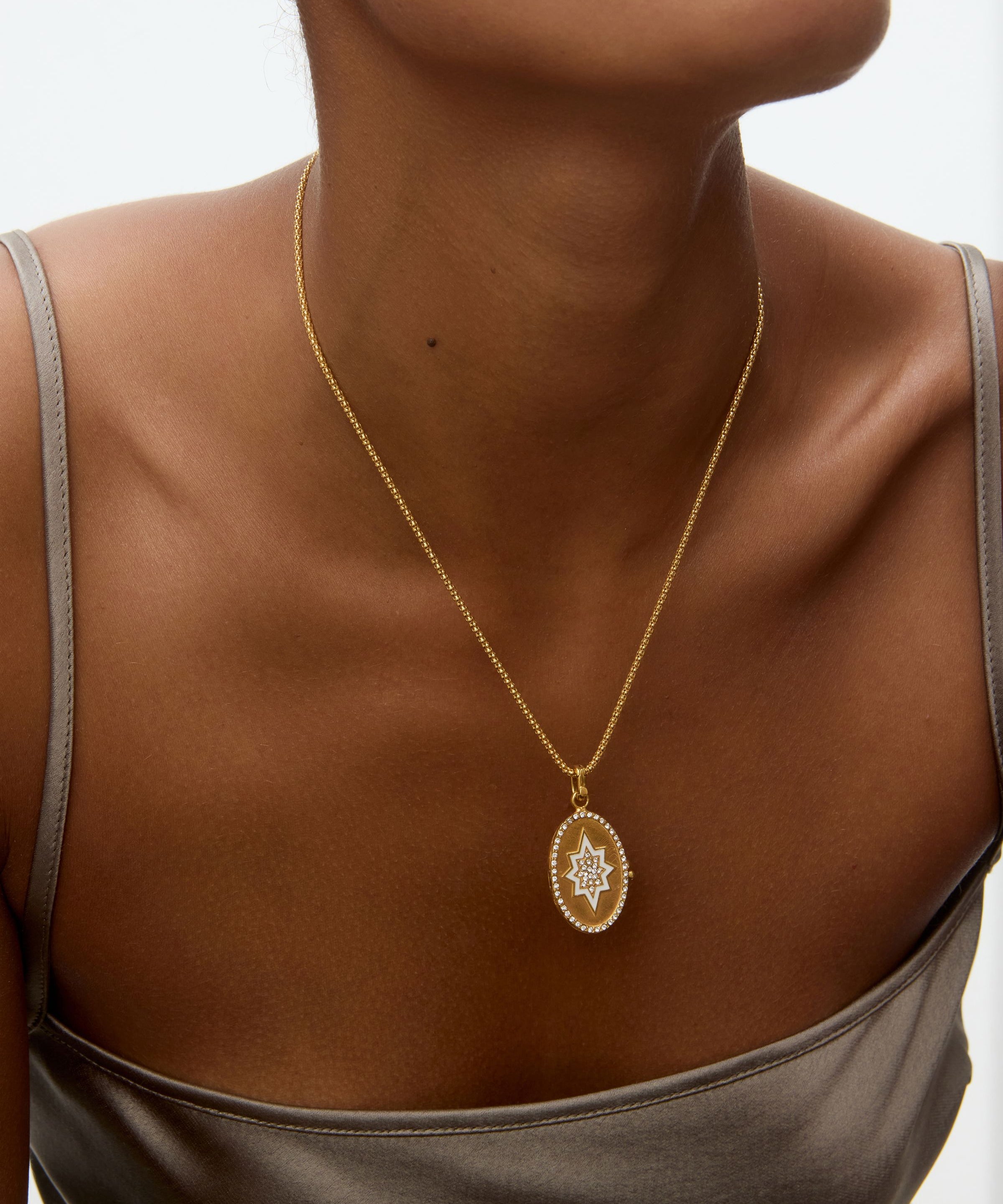 Gold necklace with a oval shaped locket pendant on a person wearing a gray top against a neutral background