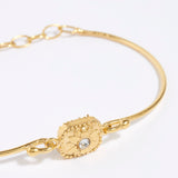 Gold bracelet with a decorative floral centre with a small crystal. set on a white background