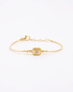 Gold bracelet with a decorative floral centre with a small crystal. set on a white background