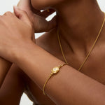 Gold bracelet on a wrist with a neutral background