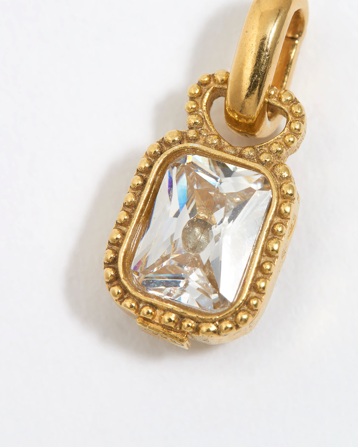 close up photo of Gold charm pendant with a clear gemstone on a white background