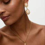 Close-up of a woman wearing gold earrings and necklace on a neutral background