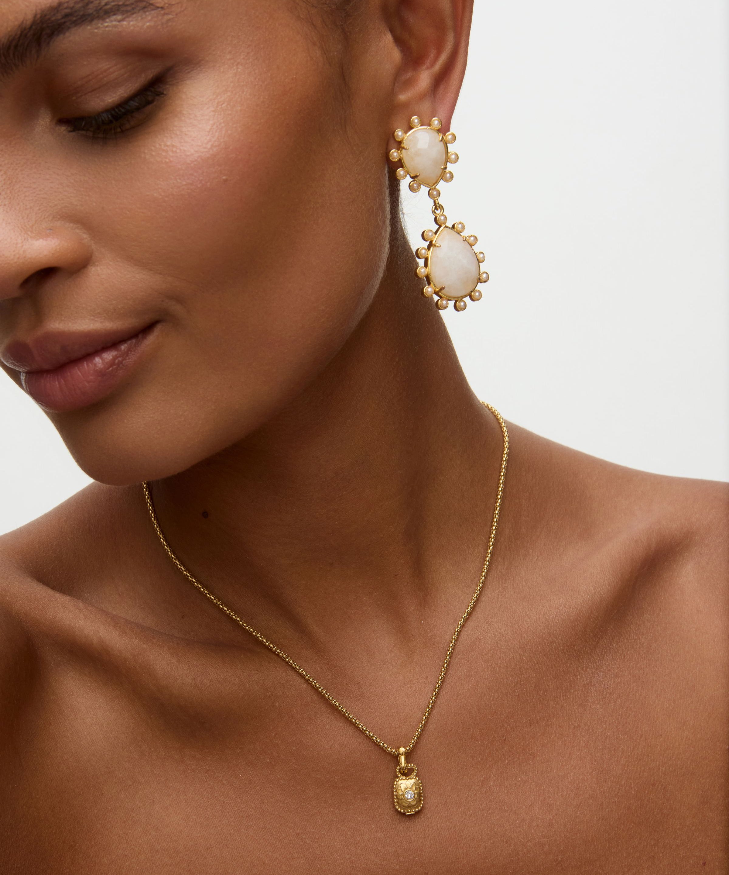 Close-up of a woman wearing gold earrings and necklace on a neutral background