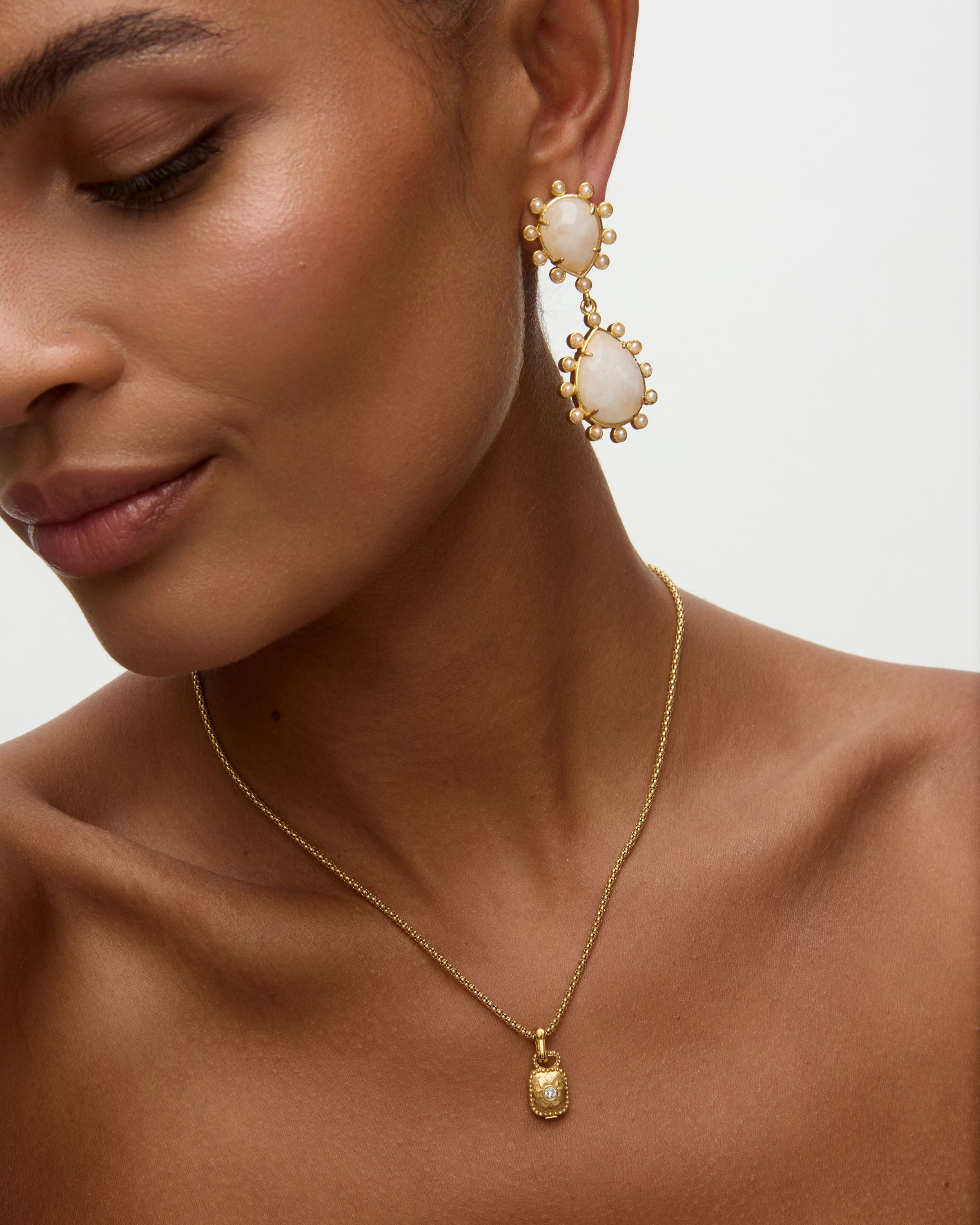 Close-up of a woman wearing gold earrings and necklace on a neutral background