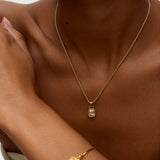 Gold necklace and bracelet on a person against a neutral background