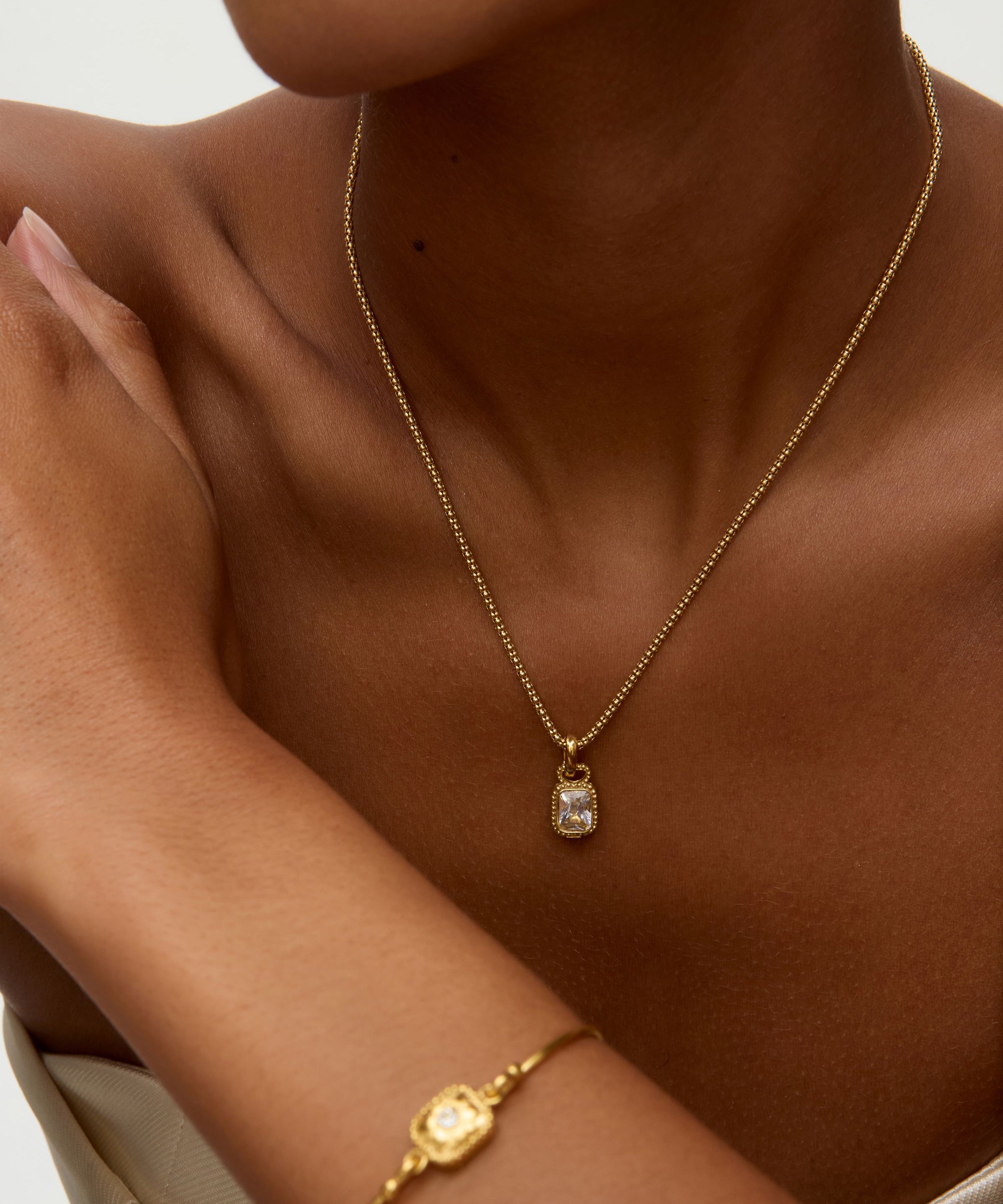 Gold necklace and bracelet on a person against a neutral background