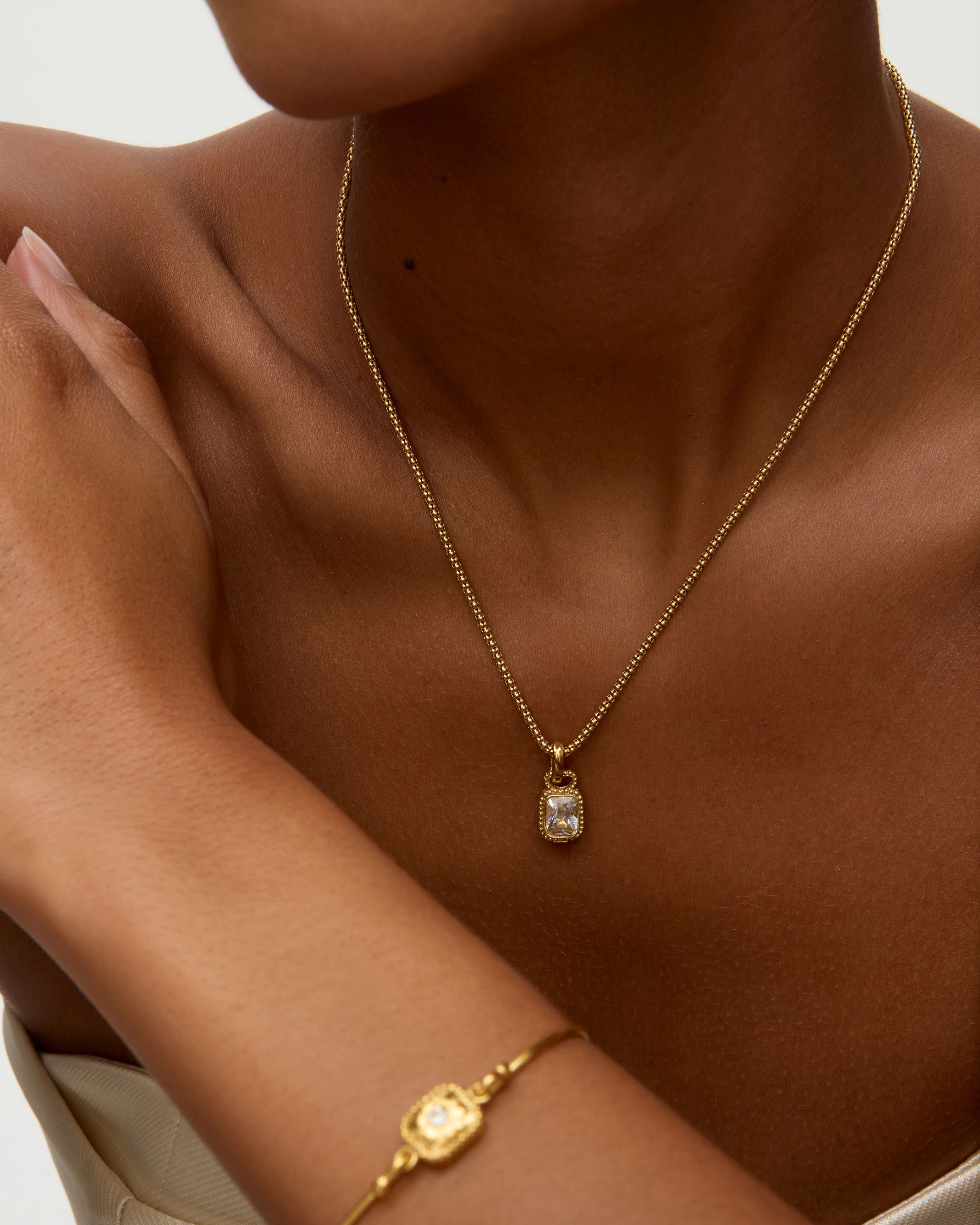 Gold necklace and bracelet on a person against a neutral background