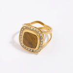 Gold ring with a square tigers eye gemstone surrounded by clear crystals on a white background