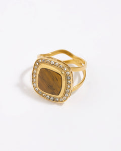 Gold ring with a square tigers eye gemstone surrounded by clear crystals on a white background