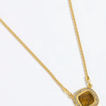 Gold necklace with a BROWN TIGERS EYE STONE SURROUNDED BY CRYSTALS ON A GOLD CHAIN on a white background