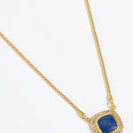 Gold necklace with a square blue pendant surrounded by crystals , on a white background