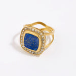 Gold ring with a blue lapis stone and clear gemstones on a white background
