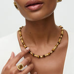 Woman wearing a gold necklace and ring and statement square earrings on a white background