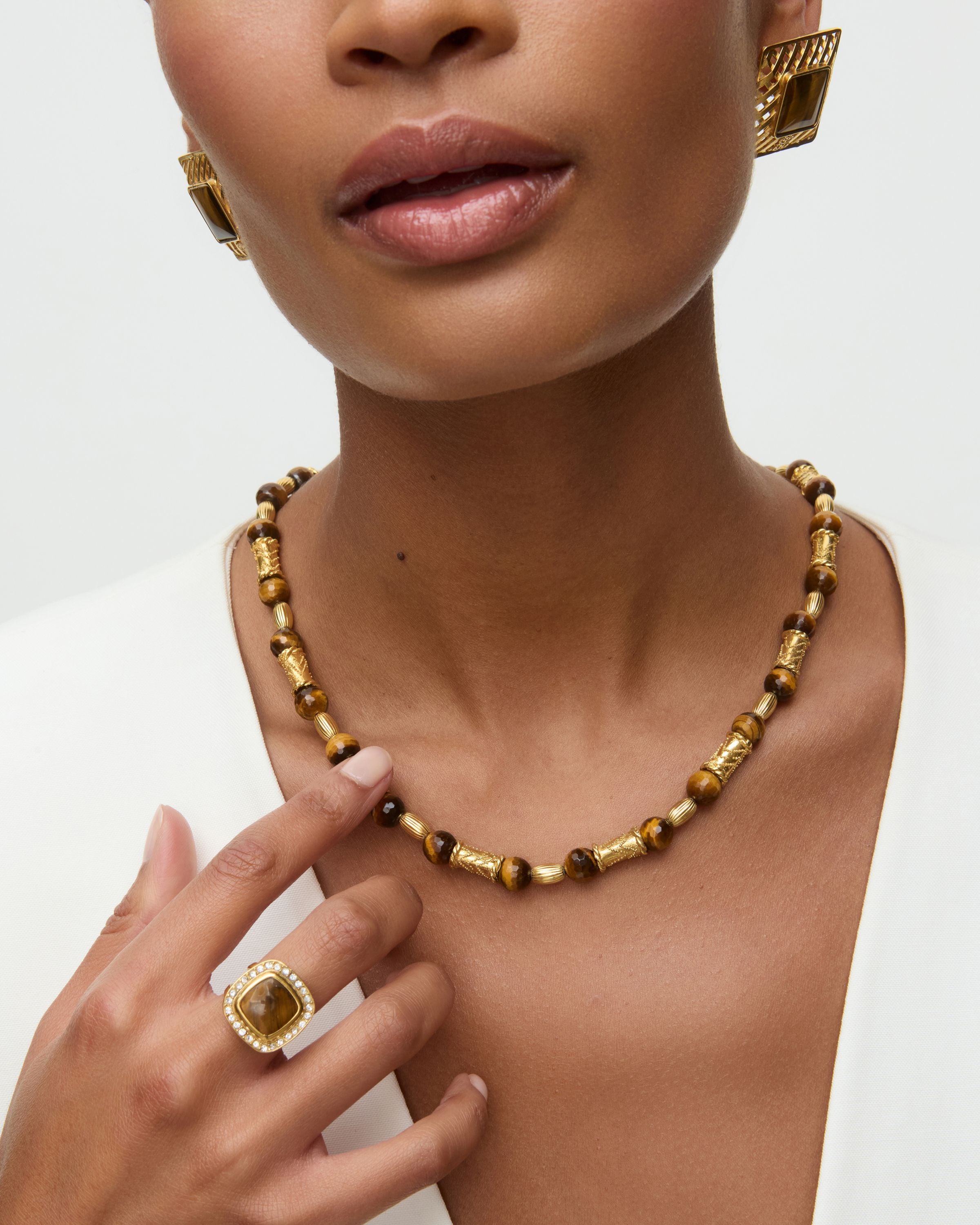 Woman wearing a gold necklace and ring and statement square earrings on a white background