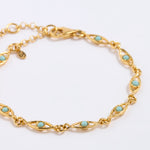 Gold bracelet with turquoise stones on a light gray background