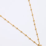 Gold coloured necklace with a small evil eye pendant on a white background