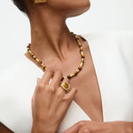 Close-up of a person wearing gold and tigers eye jewelry including a necklace, ring, and earrings on a white background.