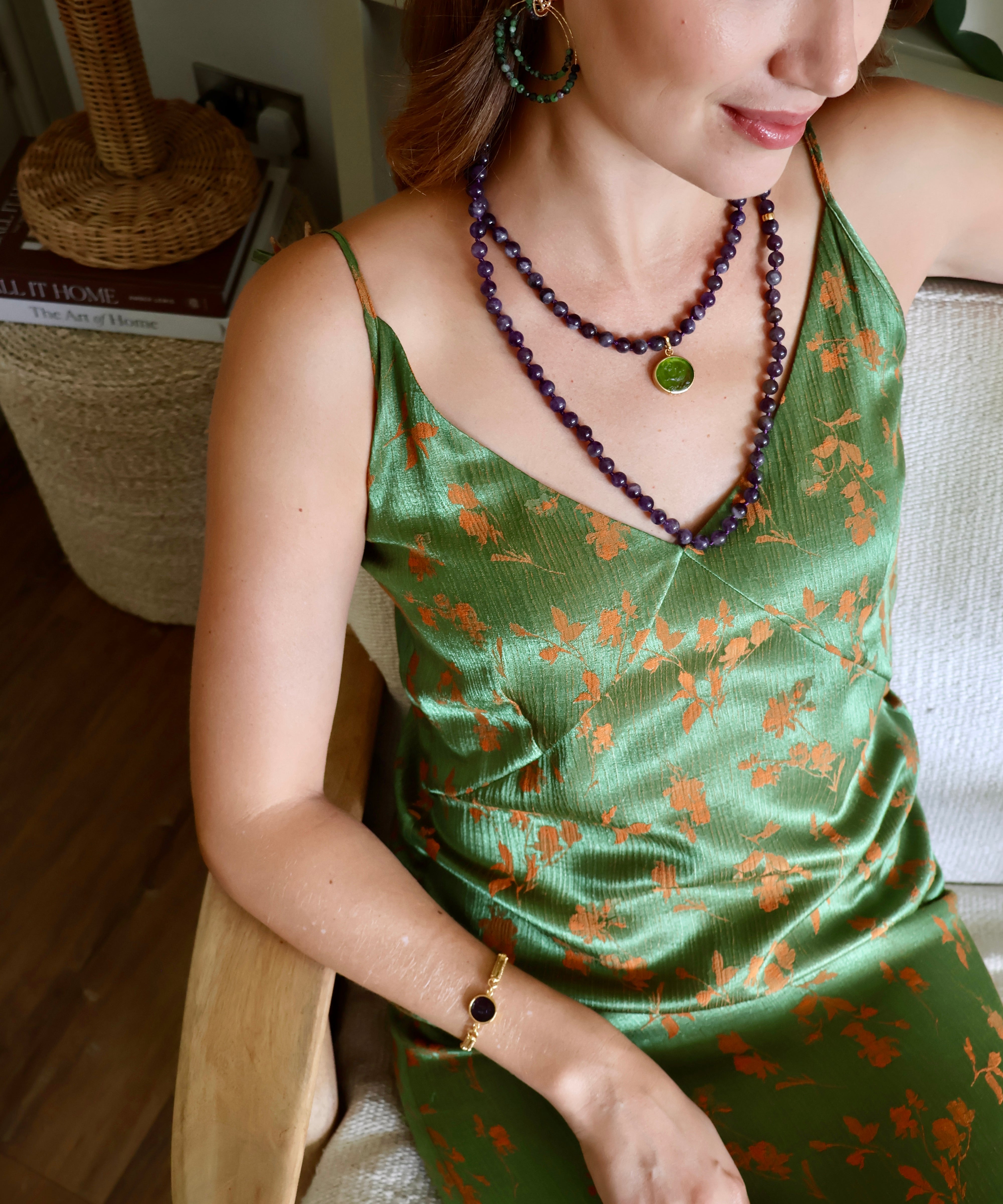 woman wearing a green strappy dress, a purple beaded necklace with a small green charm attached and purple and green beaded statement hoop earrings. 