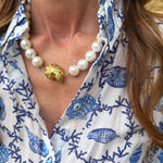 Close-up of a person wearing a blue and white patterned shirt with a pearl necklace.