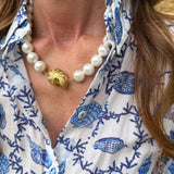 Close-up of a person wearing a blue and white patterned shirt with a pearl necklace.