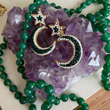 Gold crescent moon and star earrings embellished with green and white beads, displayed on a purple amethyst crystal cluster with a green beaded necklace.