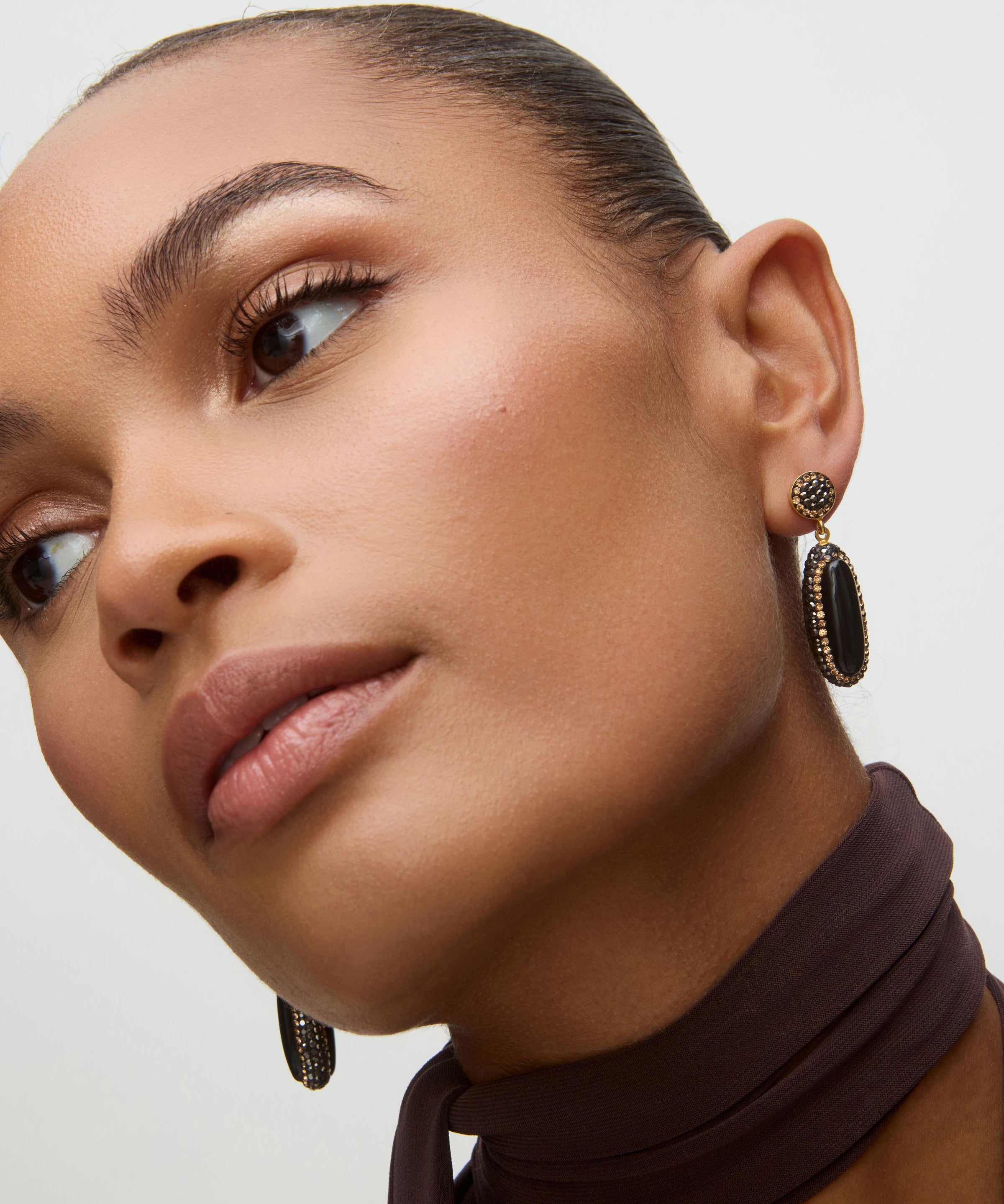Close-up of a woman wearing black onyx earrings with a neutral background