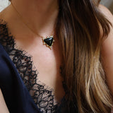 A close-up of a woman wearing a gold chain necklace with a triangular onyx pendant, styled with a black lace camisole top.