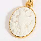 Gold coloured pendant with a white cameo on a light background
