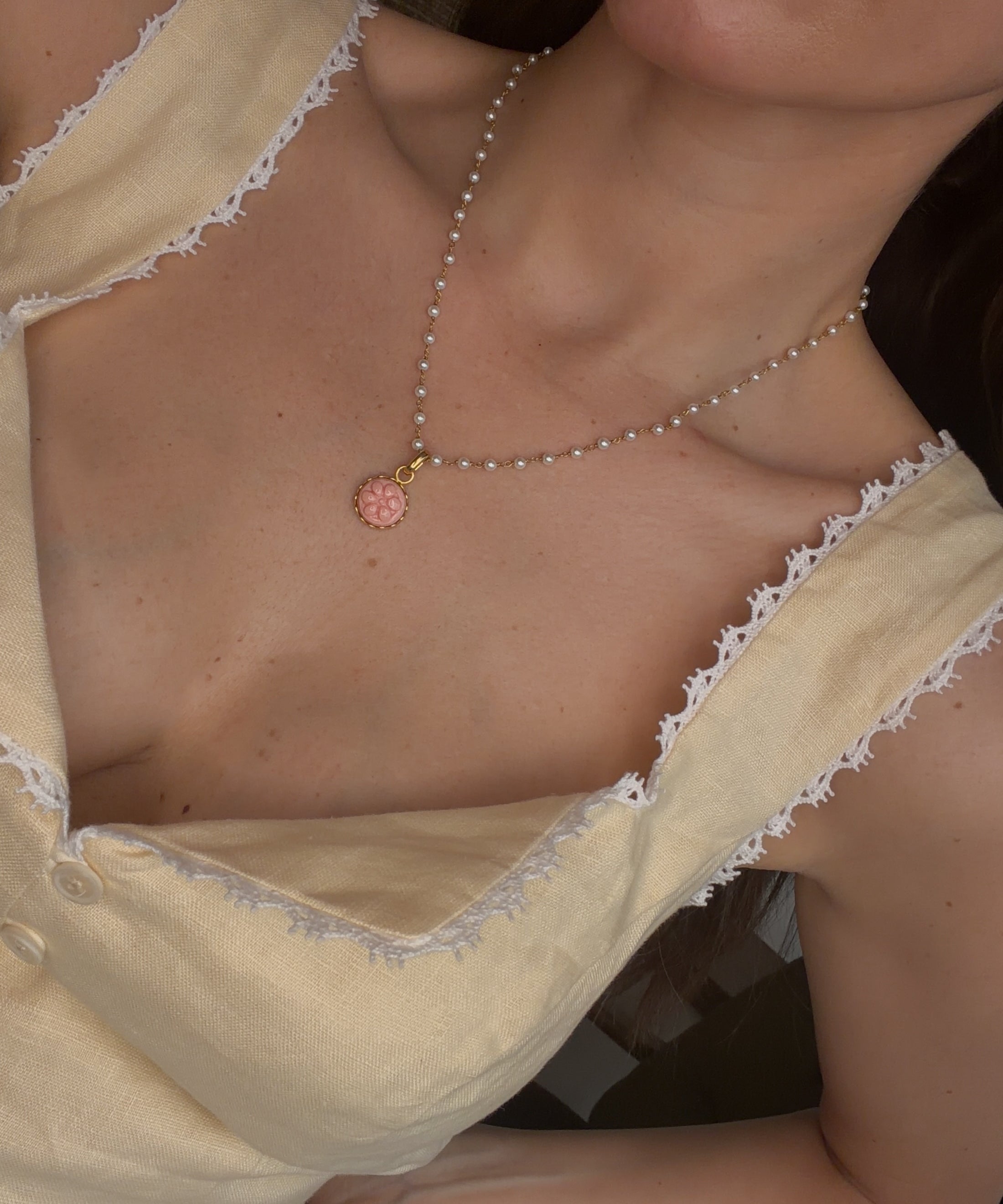 close up image of pearl beaded necklace with a pink flower design charm worn