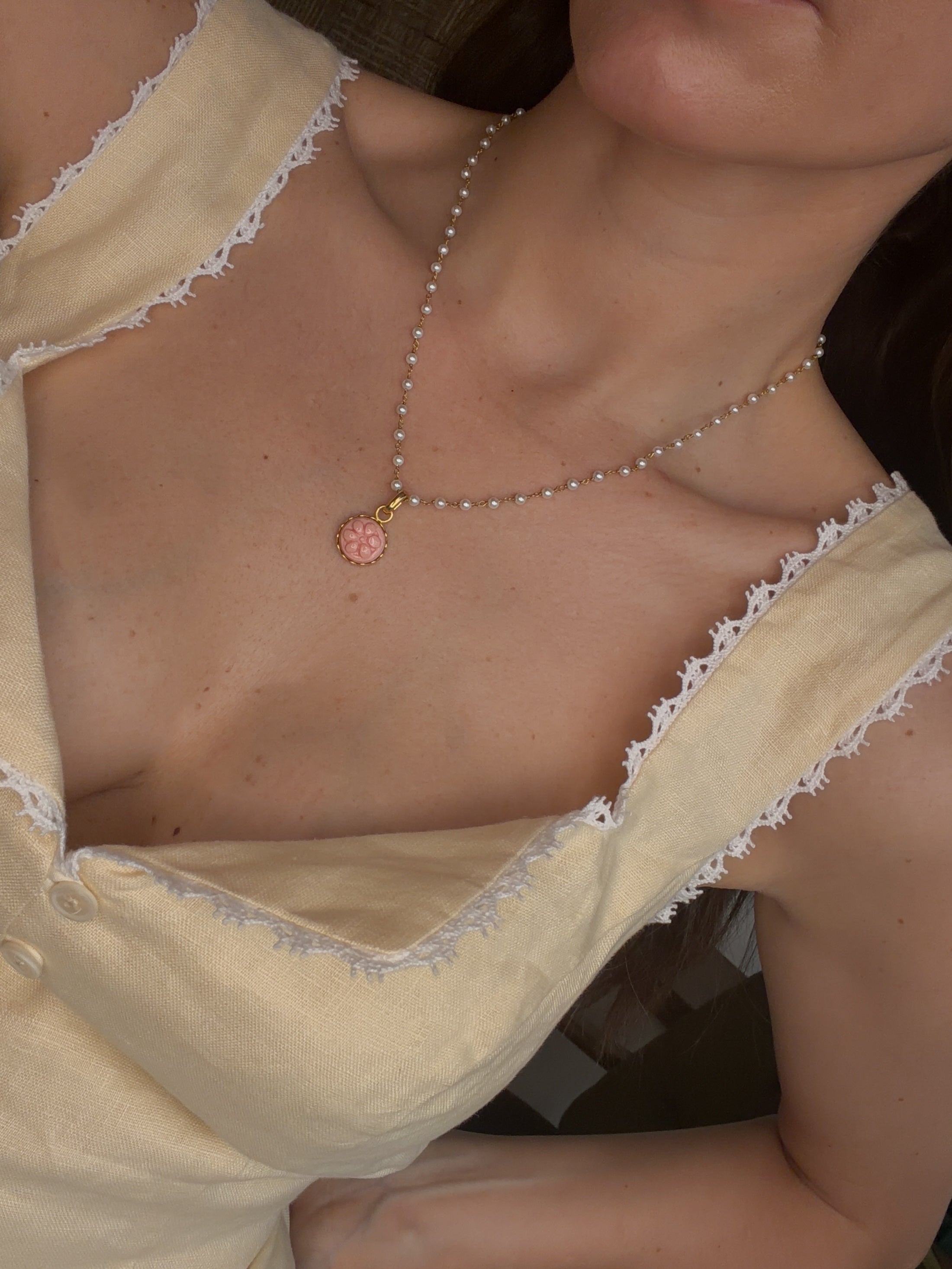 close up image of pearl beaded necklace with a pink flower design charm worn
