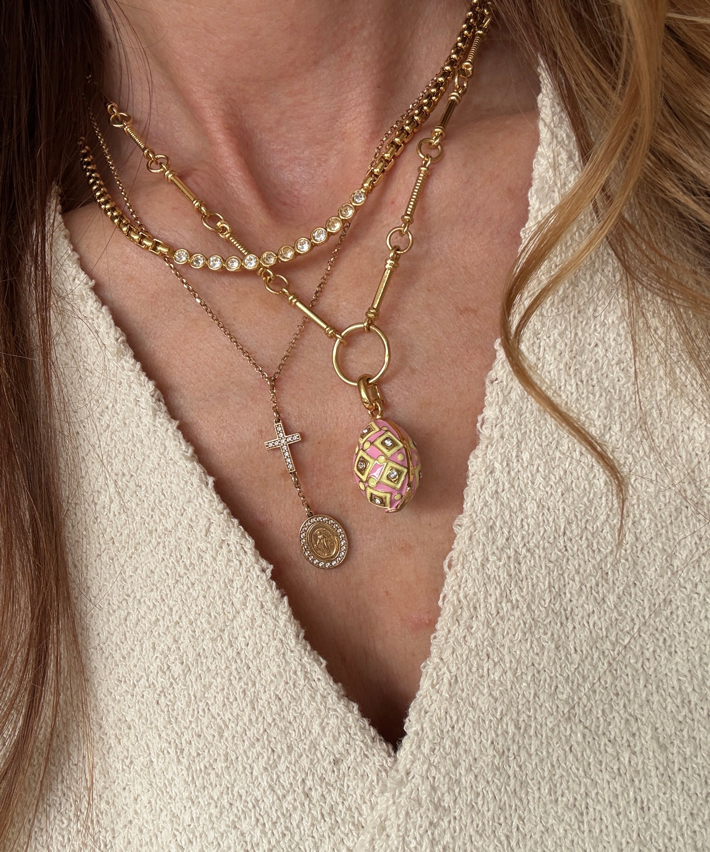showing the pink egg charm attached to a chain and worn as part of a layering of gold necklaces 