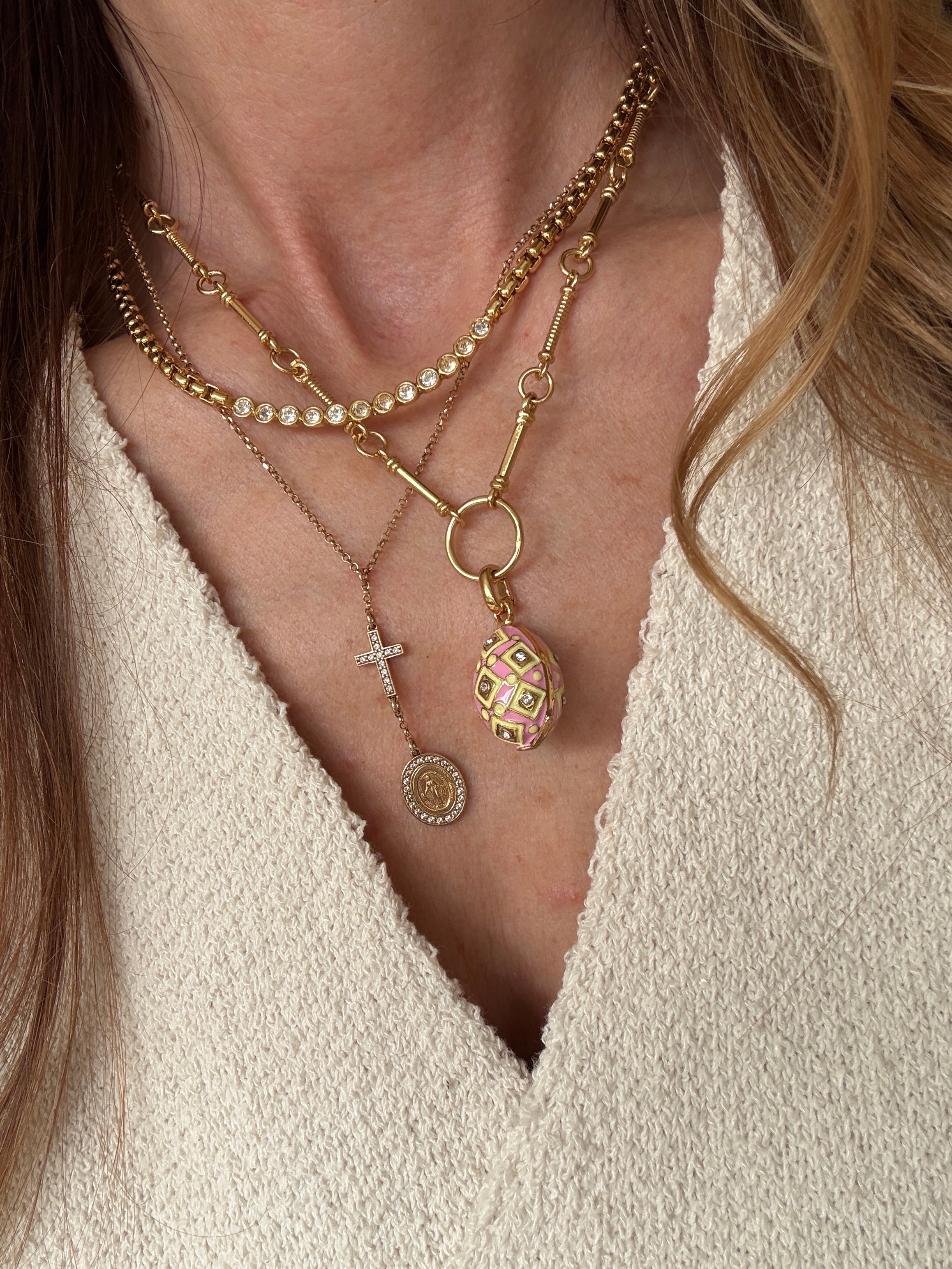 showing the pink egg charm attached to a chain and worn as part of a layering of gold necklaces 