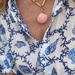 close up pink shell charm on gold chain being worn with blue shell print shirt 